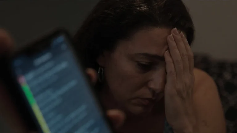 Início Mulher no sofá à noite olha o celular cheio de notificações de cobrança, com a mão na testa