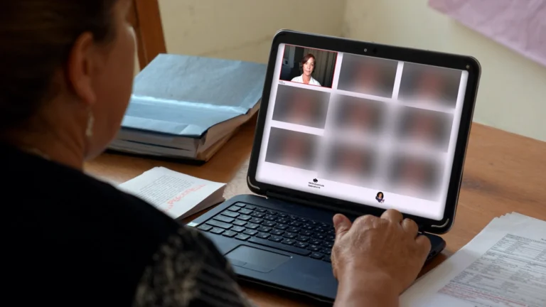 Início Mulher acompanha audiência de conciliação por vídeo no notebook, com documentos de dívidas sobre a mesa