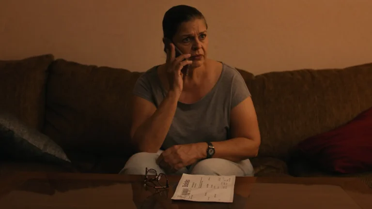 Início Mulher no sofá desconfiada durante uma ligação telefônica, com um boleto impresso sobre a mesa