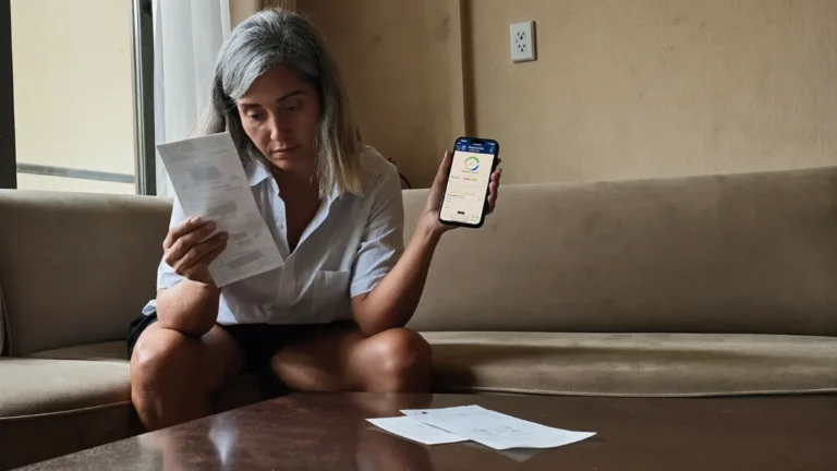 Mulher no sofá com o recibo da empresa de limpa nome e, no celular, a consulta do CPF ainda com dívidas